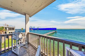 Un balcon d’où l’on peut admirer un navire bleu sur l’eau, une jetée et un bâtiment en arrière-plan.