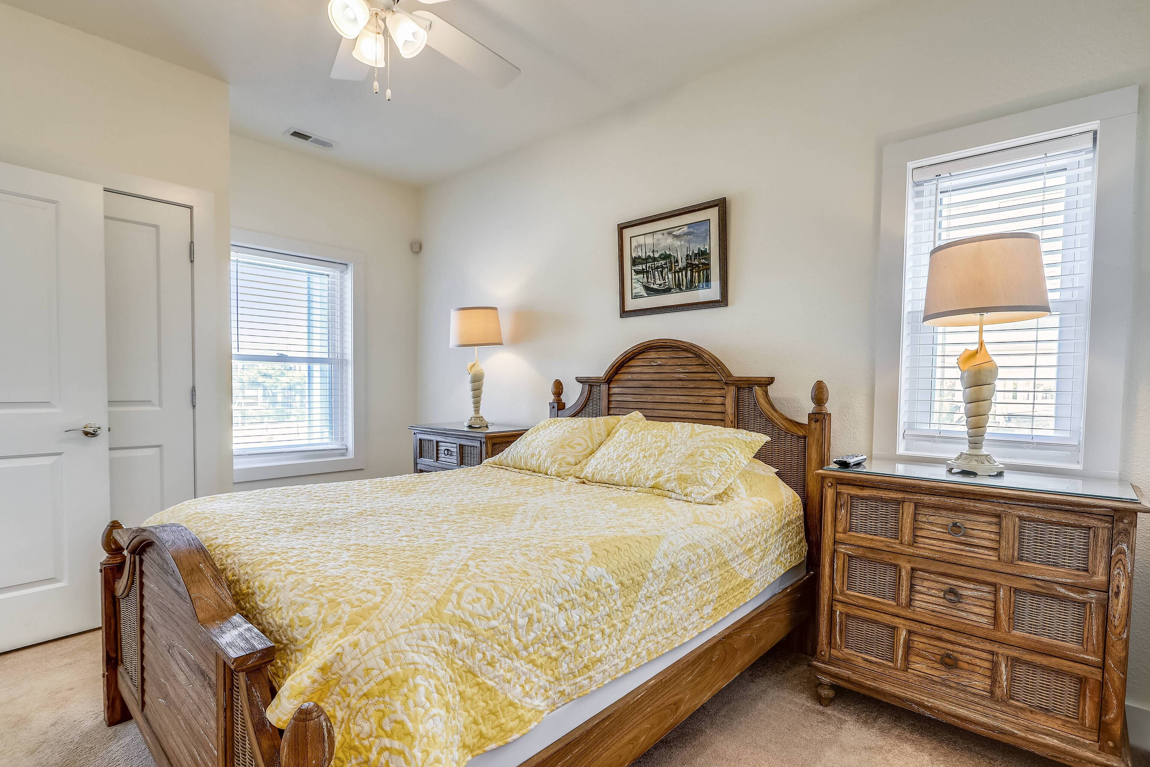 A bedroom with a bed, bedside tables, a ceiling fan, a window with blinds, and a framed picture on the wall.
