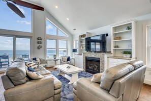 Relax in this stylish living room with a high ceiling, large windows, and a fireplace, featuring leather sofas, a flat-screen TV, and shelving.