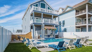 Ein zweistöckiges Haus mit Pool, Sitzgelegenheiten im Freien und einer Holzterrasse.