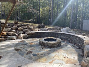 A stone fire pit surrounded by large rocks and a hammock in a forested area. - Tucked In The Woods (Pittsboro)