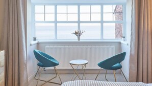 A room with a large window, two blue chairs, a small round table, and a radiator below the window.