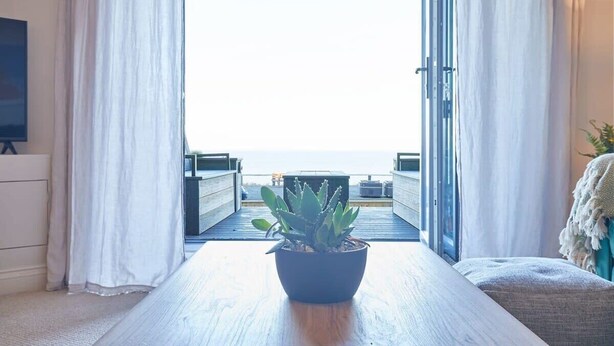 A room with a large window, a potted plant on a wooden table, and a view of the sea.