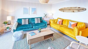 A living room with teal and yellow sofas, a wooden coffee table, and a wooden wall decoration.