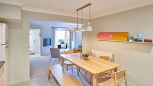 A modern kitchen with a wooden table and bench, a hanging light fixture, and a shelf with kitchenware.