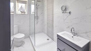 A modern bathroom with a glass-enclosed shower, a toilet, and a sink with a mirror.