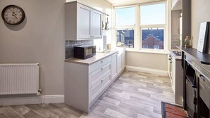 A compact kitchen with grey cabinets, a microwave, and a window overlooking a residential area.