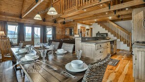 Interior de una cabaña de madera con comedor, cocina y escalera.