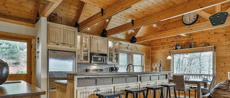 Interior de una cabaña con cocina, taburetes de bar, una mesa de comedor y un sofá de cuero.
