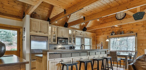 Interior de una cabaña con cocina, taburetes de bar, una mesa de comedor y un sofá de cuero.