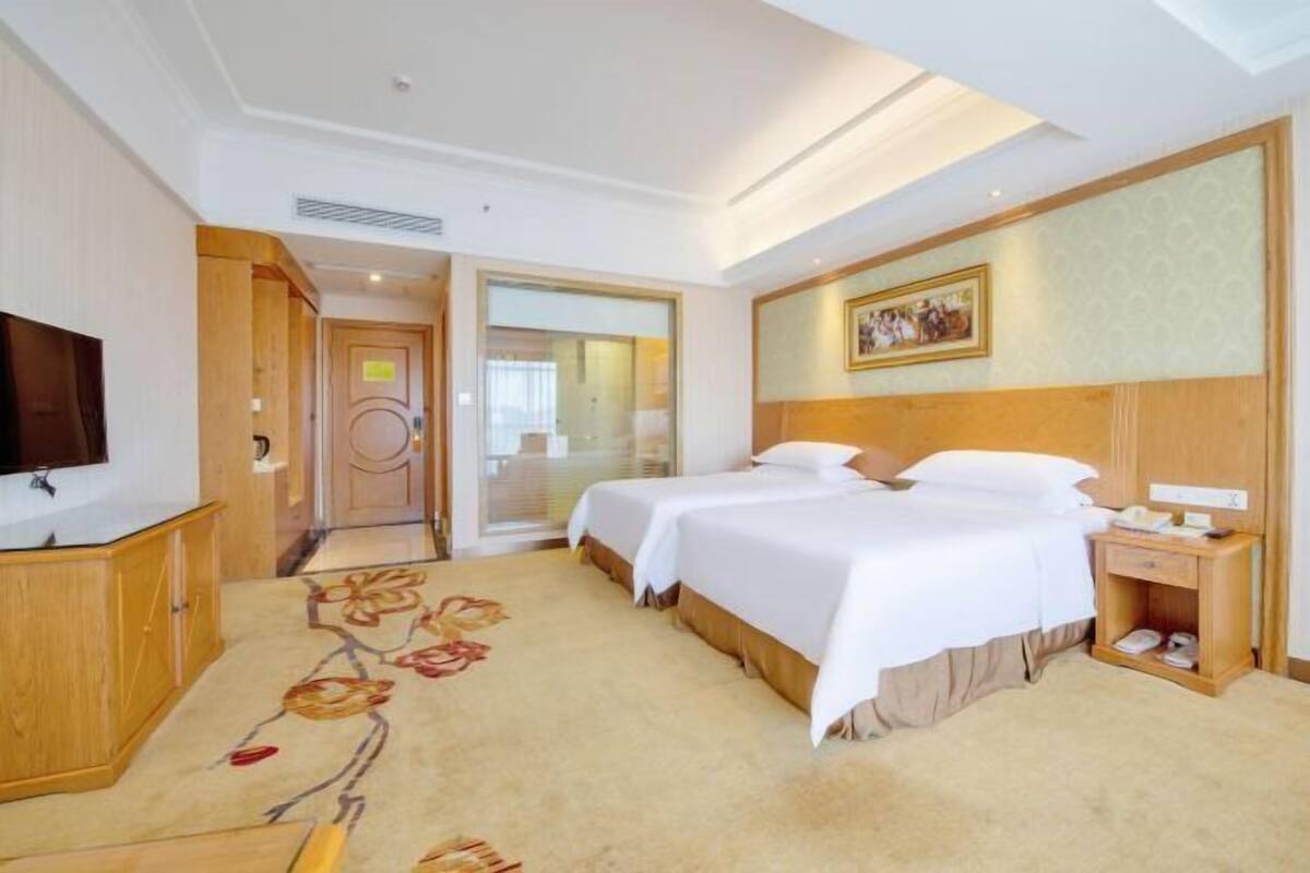 A hotel room with a bed, bedside table, TV, and a carpet with a floral pattern.