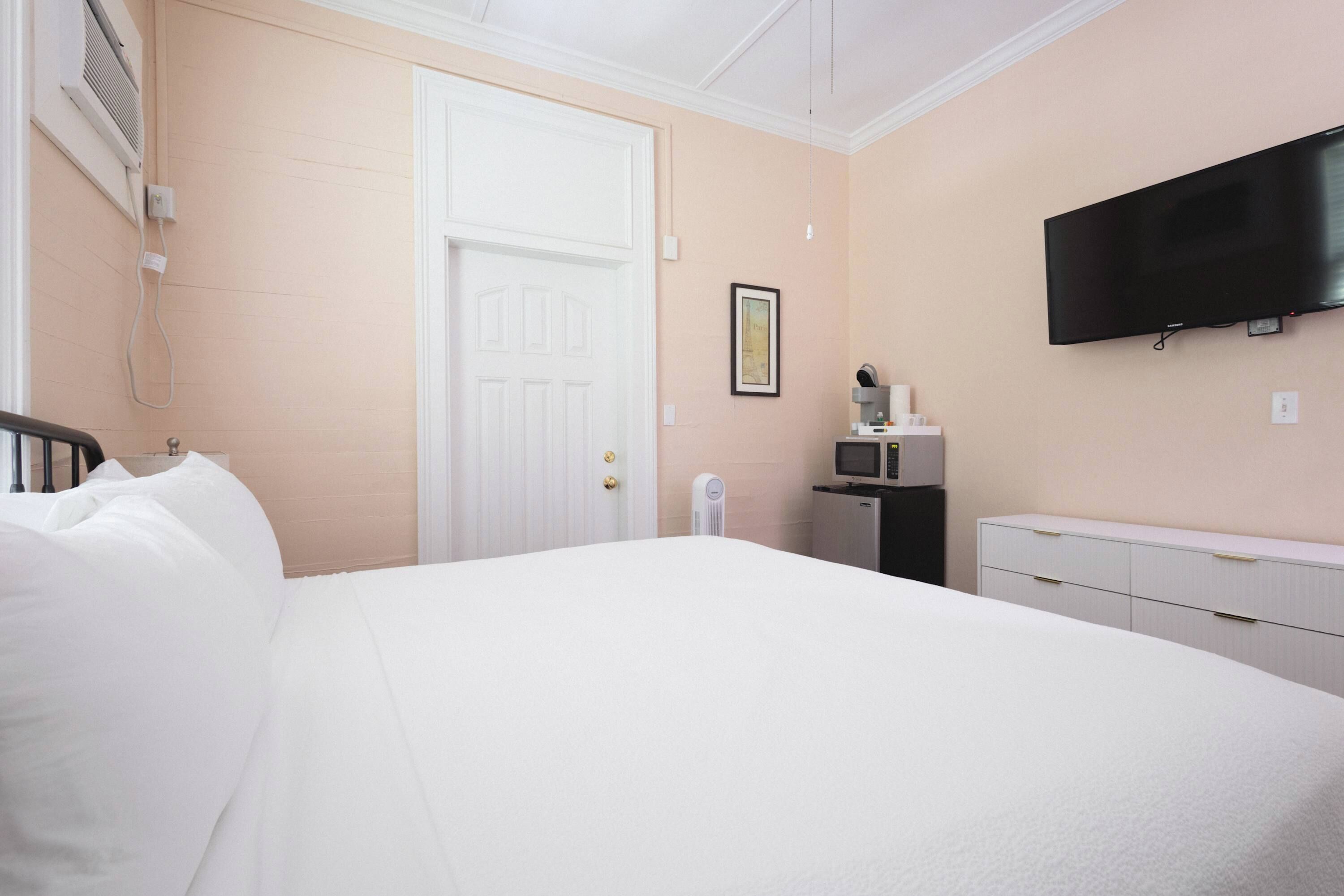 A hotel room with a bed, a TV mounted on the wall, a bedside table with a lamp, and a door.
