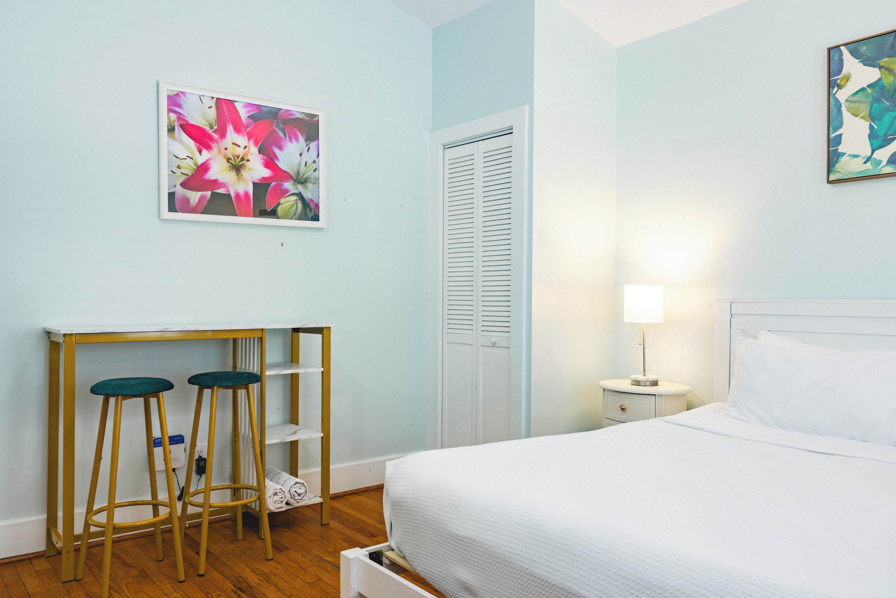 A bedroom with a bed, a nightstand, a lamp, a stool, a shelf, and a door.