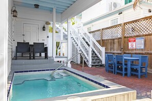 Zona de piscina con jacuzzi, asientos al aire libre y cerca de madera con normas de la piscina.