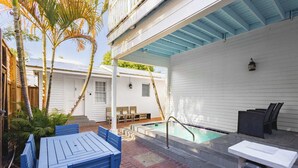 Un área junto a la piscina con una mesa y sillas azules, una piscina pequeña y un porche cubierto.