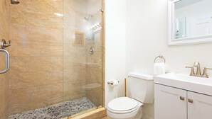 Un baño con ducha envuelta en vidrio, un inodoro y un lavabo blanco con un espejo encima.