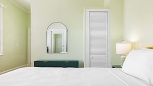 Habitación de hotel con una cama grande, un aparador verde, una puerta blanca y un espejo en la pared.