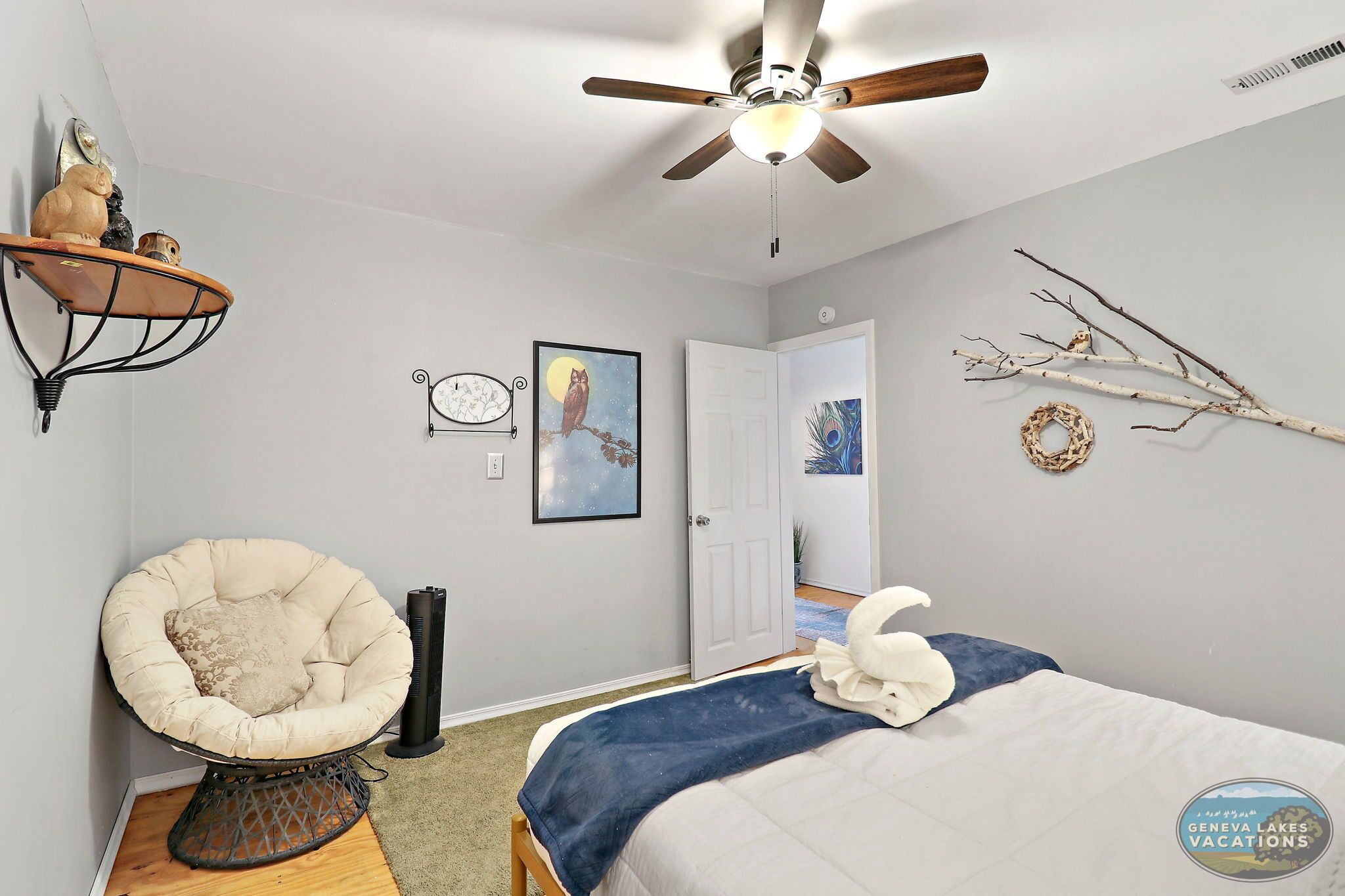 A bedroom with a bed, a chair, a ceiling fan, and wall decorations.