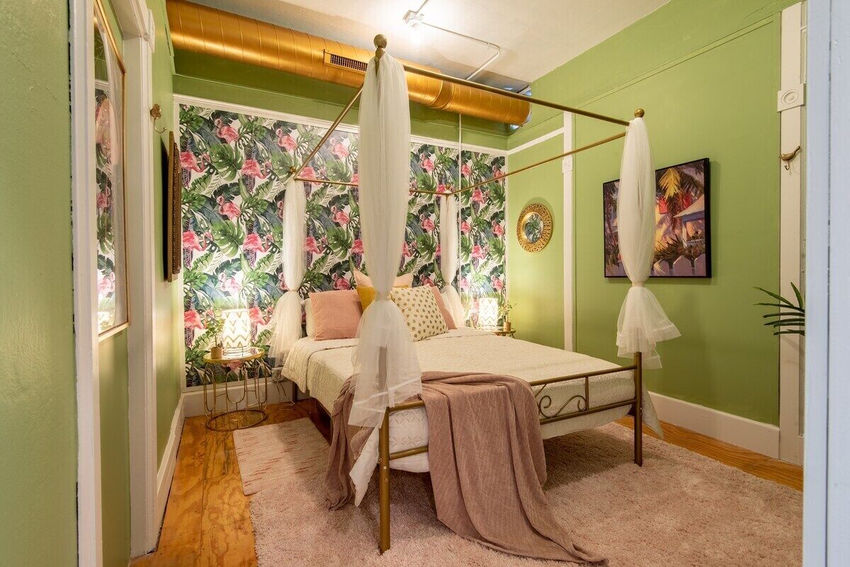 Een slaapkamer met een hemelbed, bloemenbehang en een groene wand.