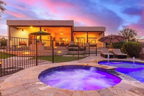 A modern outdoor pool area with a hot tub, lounge chairs, and a covered seating area.