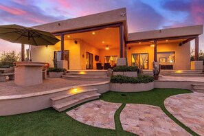 A modern house with a patio, outdoor seating, and a well-lit interior.