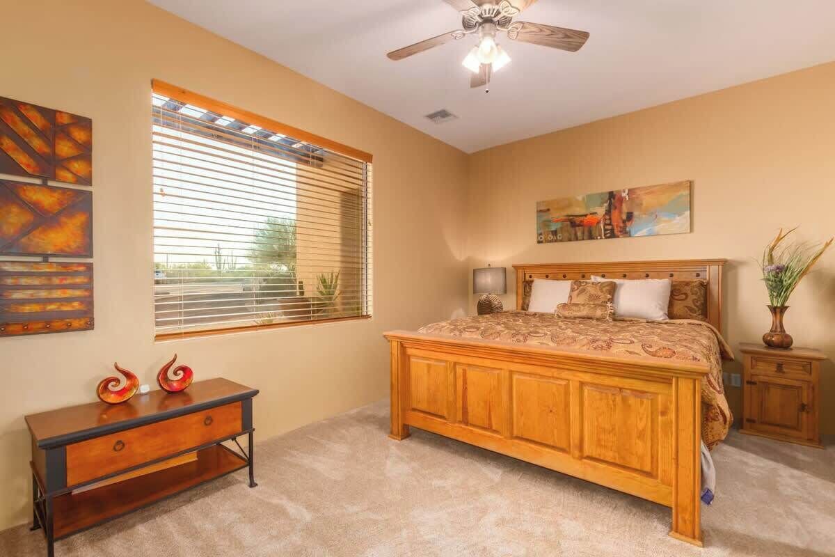 A bedroom with a wooden bed, a ceiling fan, a window with blinds, a bedside table, and a nightstand.