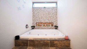A modern bathroom with a freestanding bathtub, a window above the shower, and a tiled backsplash.