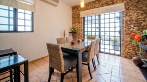 A dining area with a glass table, wicker chairs, and a view through a large window.