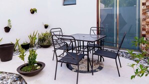 A patio area with a round table and chairs, surrounded by potted plants and a small window.