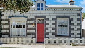 A two-story stone house with a red door, white picket fence, and a small dormer window. - Norina Cottage - circa 1858 (Port Fairy)