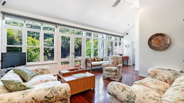 A spacious living room with large windows, a wooden coffee table, floral-patterned sofas, and a television. - Norina Cottage - circa 1858 (Port Fairy)