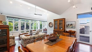 A spacious dining area with a wooden table, floral sofa, and a large window offering a view of greenery. - Norina Cottage - circa 1858 (Port Fairy)