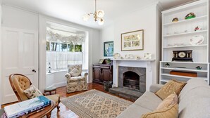 A traditional living room with a fireplace, a sofa, a chair, and a bookshelf. - Norina Cottage - circa 1858 (Port Fairy)