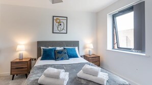 A modern hotel room with a large bed, two bedside tables with lamps, a window with curtains, and a framed abstract artwork on the wall. - Stylish 2BR Apartment | Stay Zeni, Ouse Court York (York)