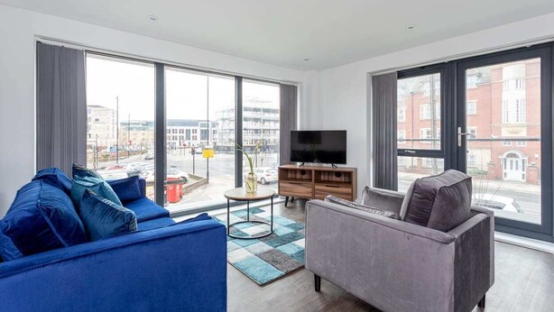 A modern living room with a large window, a flat-screen TV, a grey sofa, and a blue sofa. - Stylish 2BR Apartment | Stay Zeni, Ouse Court York (York)
