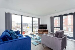 A modern living room with a large window, a flat-screen TV, a grey sofa, and a blue sofa. - Stylish 2BR Apartment | Stay Zeni, Ouse Court York (York)