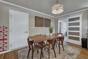 A dining area with a wooden table, six chairs, a clock, and a potted plant.