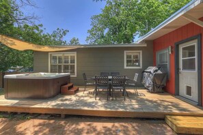 A hot tub, patio table, chairs, and a grill area in a backyard.