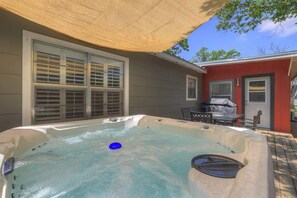 A hot tub in a backyard with a covered patio, a table, and chairs.