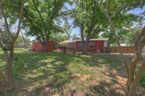 A red house with a patio area, surrounded by trees and a fenced yard.