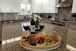 A kitchen with granite countertops, white cabinets, a stainless steel range hood, and a decorative backsplash. - Modern Comfort-Hot tub, Firepit, Mins to Downtown! (Fredericksburg)
