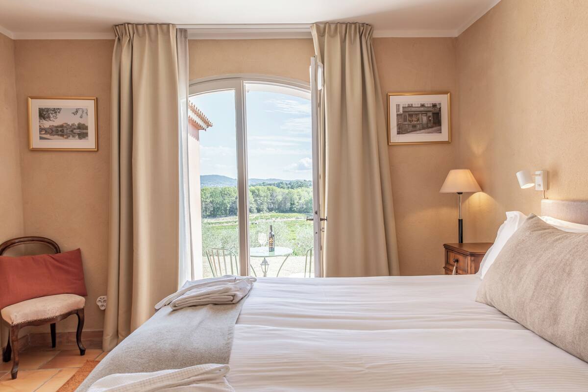 A hotel room with a large bed, a chair, a table, and a view of the outdoors.