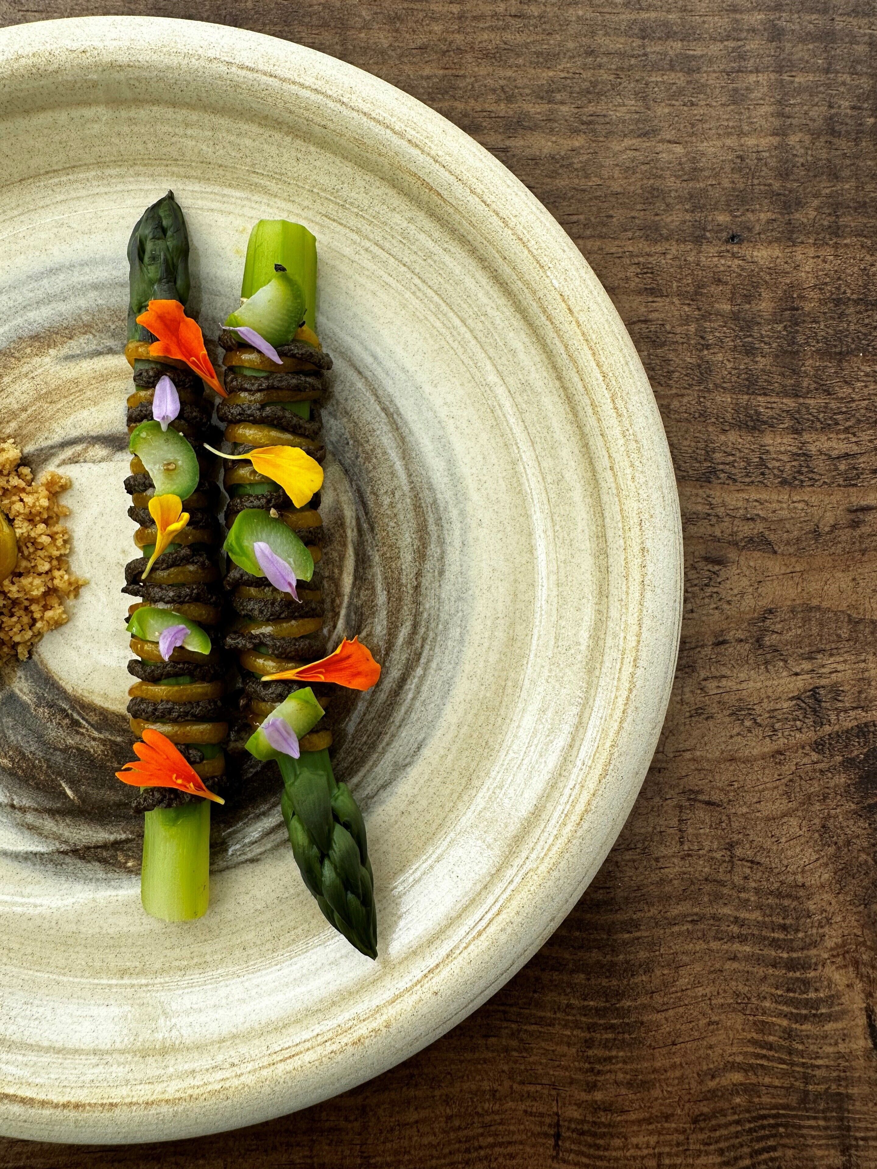 A plate with a food arrangement featuring asparagus and colorful flowers.