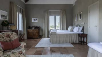 Een slaapkamer met een groot bed, een stoel, een dressoir en een raam met gordijnen.