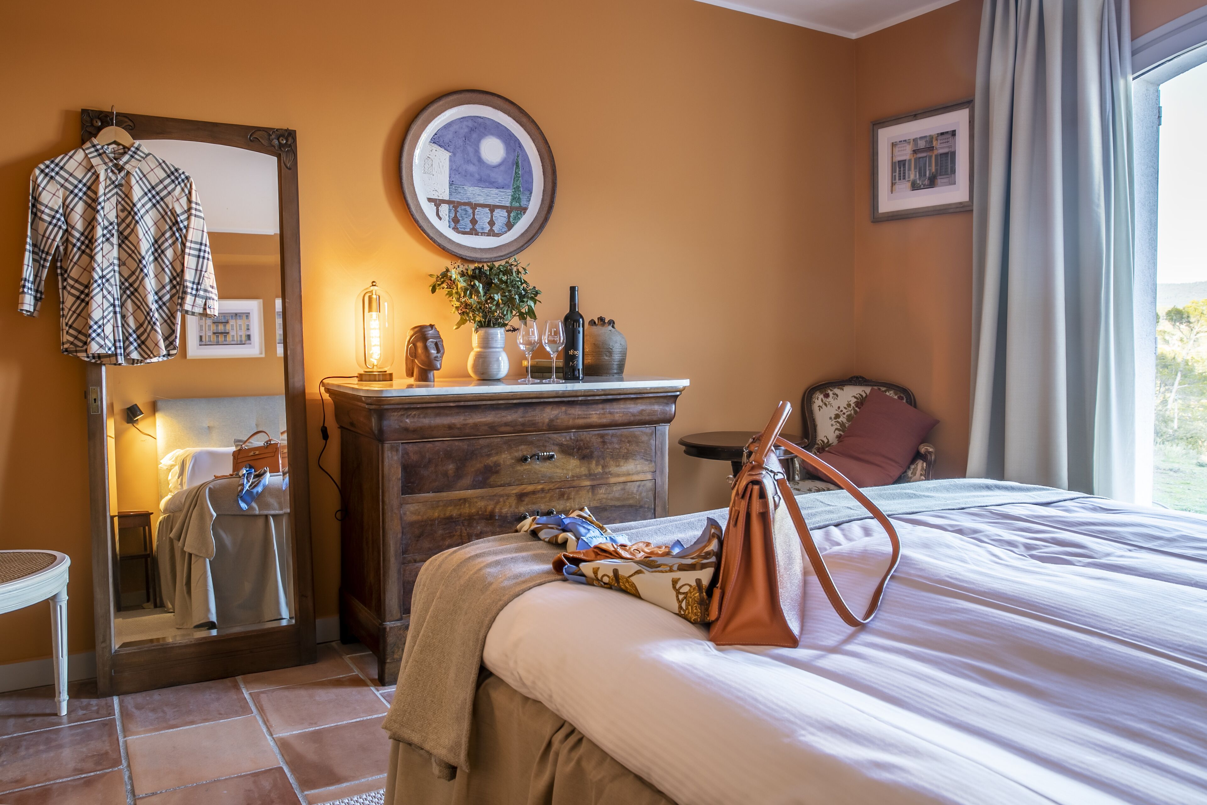 Une chambre d’hôtel avec un lit, une commode, un miroir, une table de chevet et une fenêtre avec des rideaux.