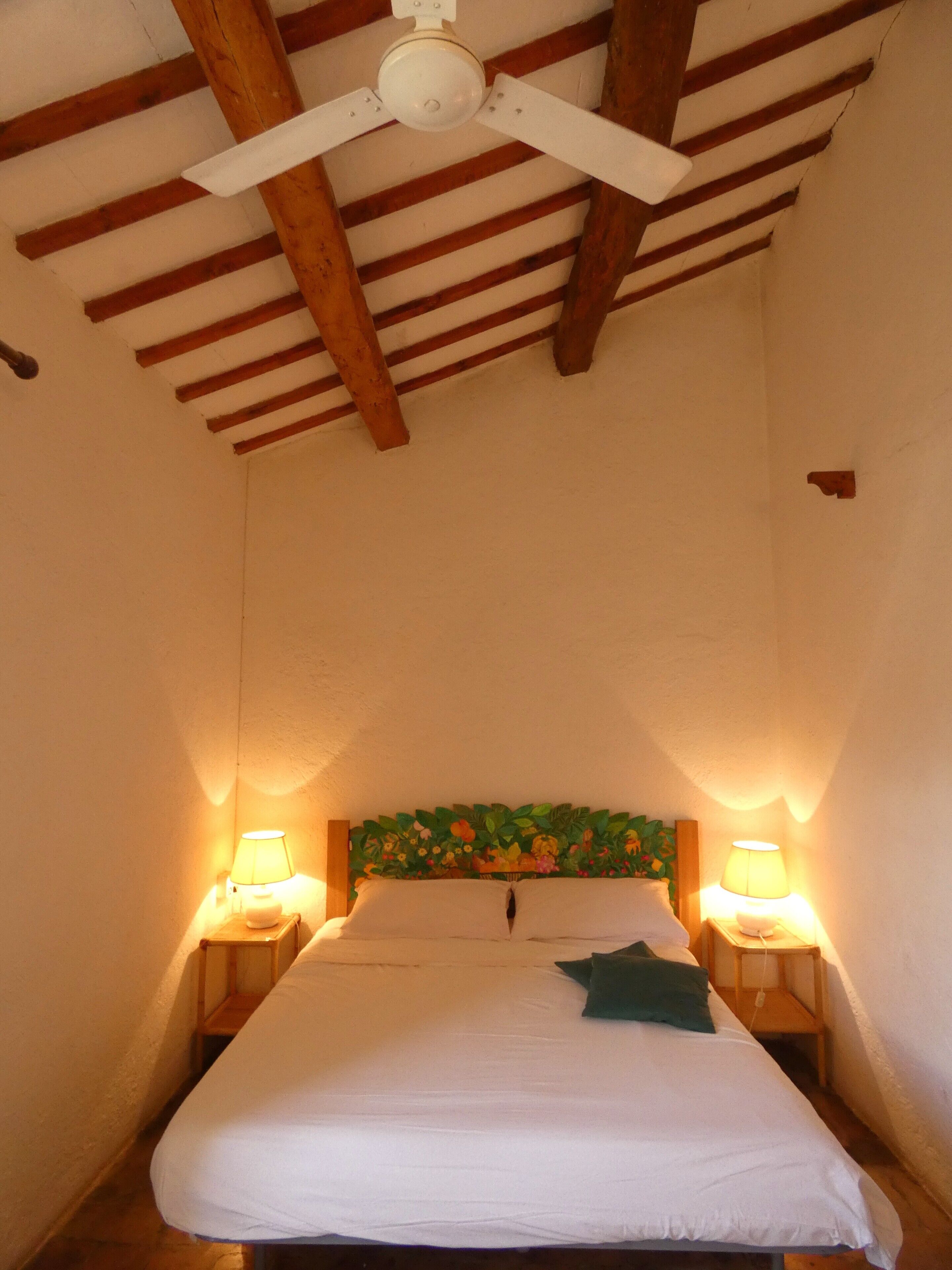 A bedroom with a wooden ceiling, a bed with white bedding, two bedside lamps, and a floral headboard.