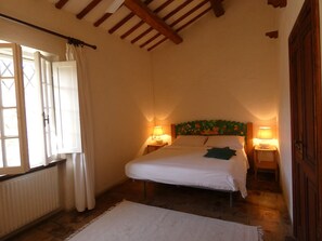 Une chambre à coucher avec un lit, deux lampes de chevet, une fenêtre avec des rideaux, un radiateur et un plafond en bois.