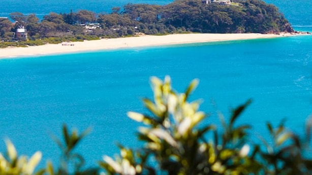 Un paysage côtier avec une plage de sable et une petite île couverte d’une végétation luxuriante.