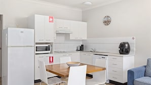 Une cuisine moderne avec des meubles blancs, un four à micro-ondes, une machine à café et un lave-vaisselle. Un panneau indiquant l’emplacement d’une couverture anti-feu et d’un extincteur est apposé sur les meubles.