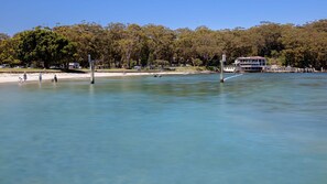 Una propiedad frente al agua con playa, un muelle para barcos y una casa grande con balcón con vistas al agua.